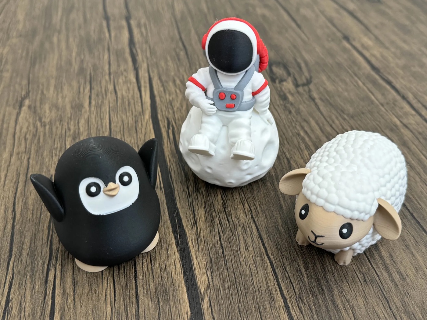 Three small multi-color 3D prints - a penguin, an astronaut, and a sheep - each printed in several filament colors